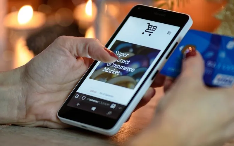 Hand using a smartphone checkout page with a bank card nearby