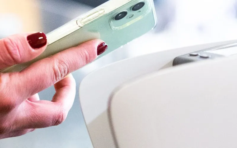 Hand holding a smartphone against a card payment terminal